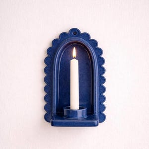 Peut inclure: Un bougeoir mural en c&eacute;ramique bleu marine avec un bord festonn&eacute;. Une bougie blanche est allum&eacute;e &agrave; l'int&eacute;rieur du support. Le bougeoir a une petite &eacute;tag&egrave;re pour tenir la bougie et un trou en haut pour l'accrocher.