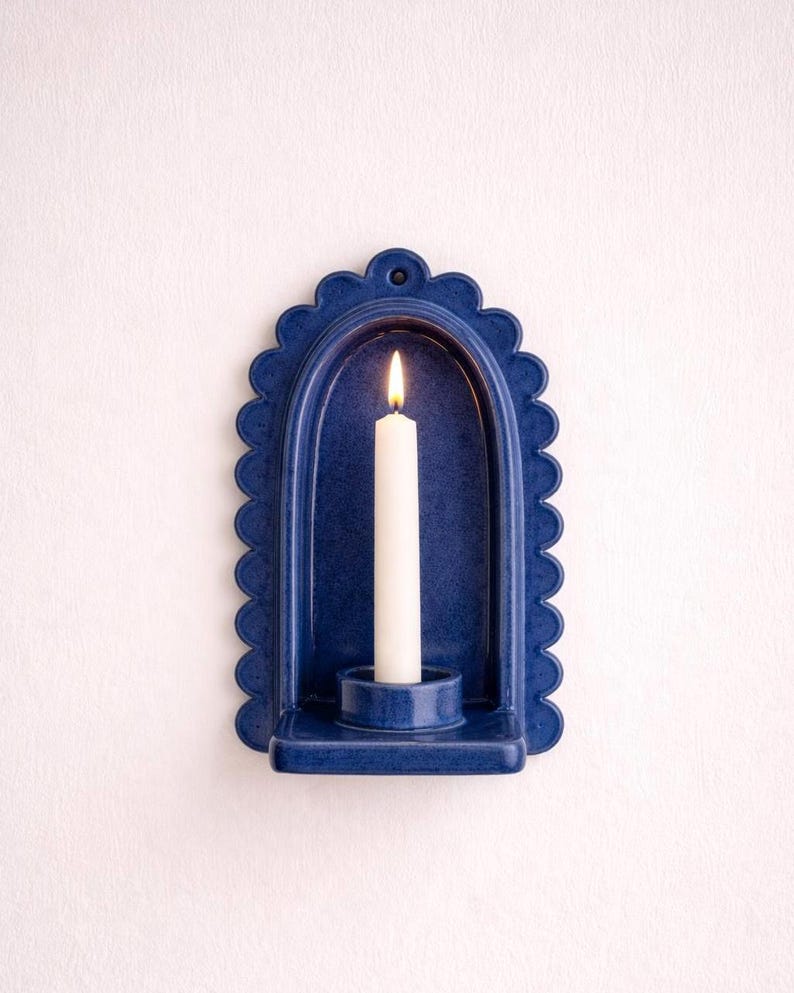 Peut inclure: Un bougeoir mural en c&eacute;ramique bleu marine avec un bord festonn&eacute;. Une bougie blanche est allum&eacute;e &agrave; l'int&eacute;rieur du support. Le bougeoir a une petite &eacute;tag&egrave;re pour tenir la bougie et un trou en haut pour l'accrocher.