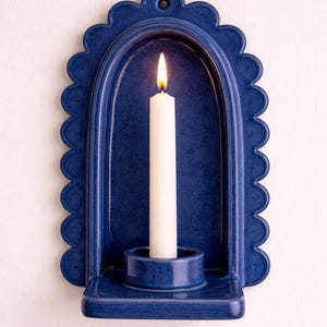 Peut inclure: Un photophore mural en c&eacute;ramique bleu marine avec un bord festonn&eacute;. Une bougie blanche est allum&eacute;e &agrave; l'int&eacute;rieur du photophore. Le photophore a un porte-bougie int&eacute;gr&eacute; et un petit trou en haut pour l'accrocher. Le design est simple et &eacute;l&eacute;gant.