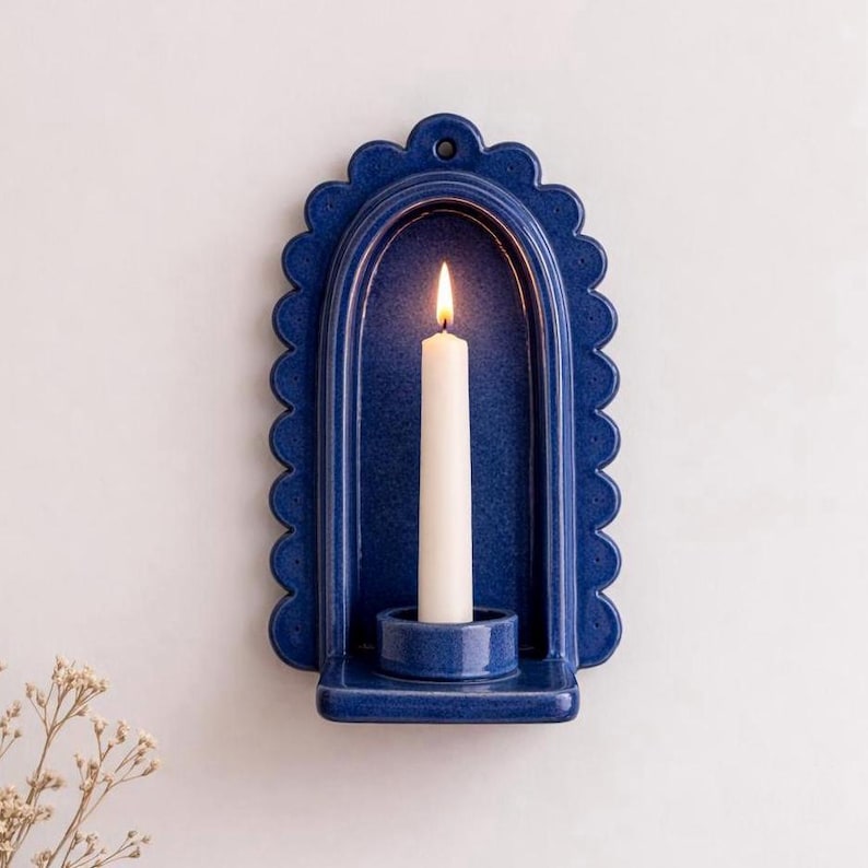 Peut inclure: Un bougeoir mural en c&eacute;ramique bleu marine avec un bord festonn&eacute;. Une bougie blanche est allum&eacute;e &agrave; l'int&eacute;rieur du support. Le bougeoir a une petite &eacute;tag&egrave;re en bas pour tenir la bougie.