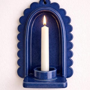 Peut inclure: Un bougeoir mural en c&eacute;ramique bleue avec un bord festonn&eacute;. Une bougie blanche est allum&eacute;e &agrave; l'int&eacute;rieur du support. Le support a un petit crochet en m&eacute;tal pour l'accrocher. Le bougeoir est un &eacute;l&eacute;ment de d&eacute;coration int&eacute;rieure.