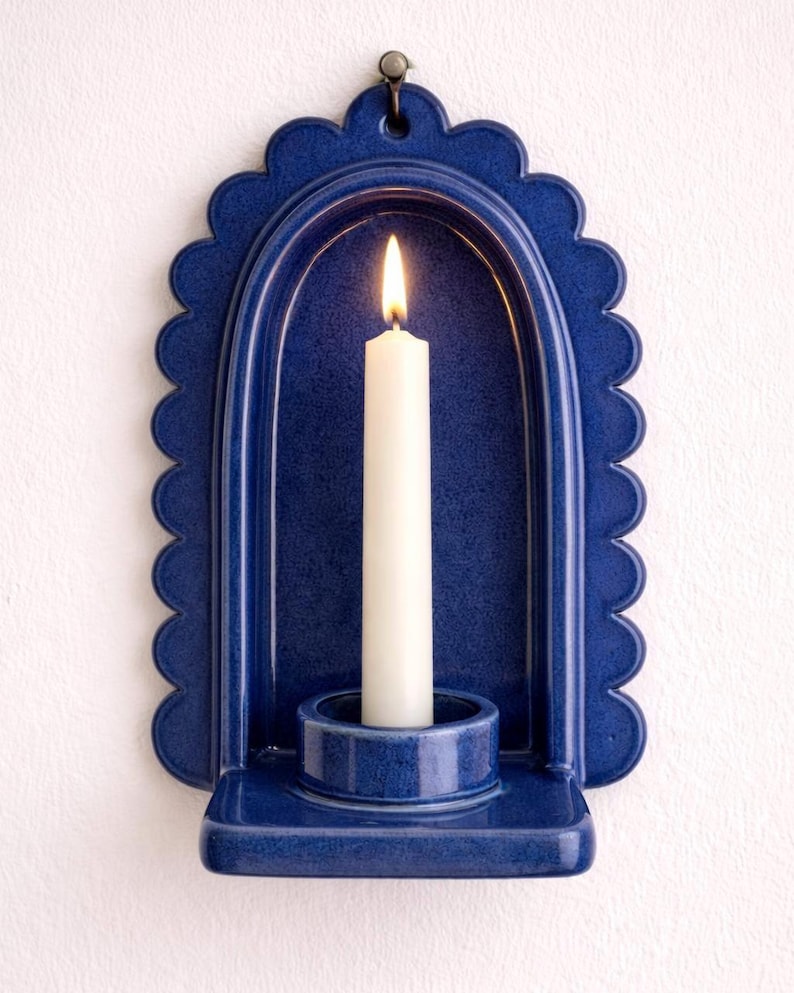 Peut inclure: Un bougeoir mural en c&eacute;ramique bleue avec un bord festonn&eacute;. Une bougie blanche est allum&eacute;e &agrave; l'int&eacute;rieur du support. Le support a un petit crochet en m&eacute;tal pour l'accrocher. Le bougeoir est un &eacute;l&eacute;ment de d&eacute;coration int&eacute;rieure.