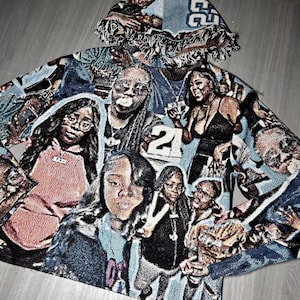 May include: A hooded tapestry jacket featuring a collage of images in shades of blue, black, and tan. The jacket has a fringed hood and a repeating pattern of faces and numbers. The overall design is a unique and artistic statement piece.
