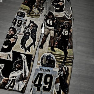 May include: Tapestry-style pants featuring a repeating pattern of football players in action. The players wear jerseys with the number 49. The color palette includes shades of gray, black, and tan.
