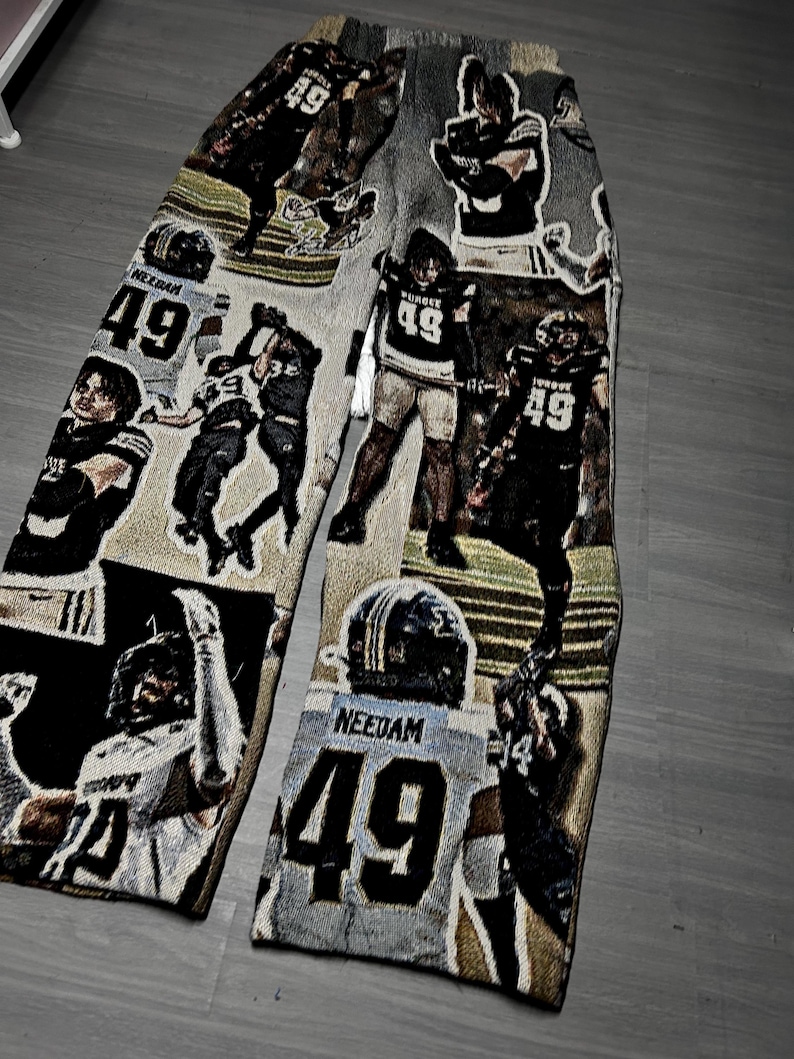 May include: Tapestry-style pants featuring a repeating pattern of football players in action. The players wear jerseys with the number 49. The color palette includes shades of gray, black, and tan.