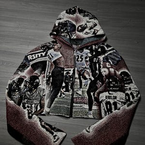 May include: Cropped zip-up hoodie with a tapestry design depicting football players. The jacket, with a hood, is predominantly black, white, and burgundy. The word "RSITY" is visible on the front.
