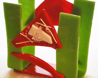 May include: A red and green glass napkin holder with a white and iridescent glass accent. The holder is made of thick, textured glass and has a modern, abstract design.