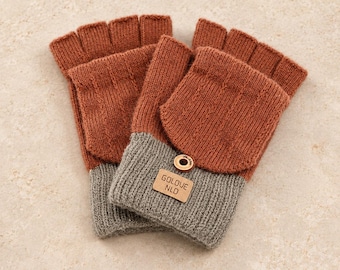 May include: A pair of fingerless gloves featuring a rust-orange knitted upper section and a grey knitted cuff. A small rectangular tan leather patch is stitched onto the cuff, displaying the text GOLOVE NLD, secured by a single metallic button.