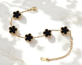 Puede incluir: Un brazalete de cadena dorada con cinco dijes en forma de flor negra. El brazalete tiene un cierre de langosta.