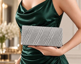 May include: A rectangular silver clutch bag with a textured, glittery finish and diagonal pleated lines. The accessory features a structured, elongated shape with a metallic sheen, designed to be held in the hand as a formal evening piece.