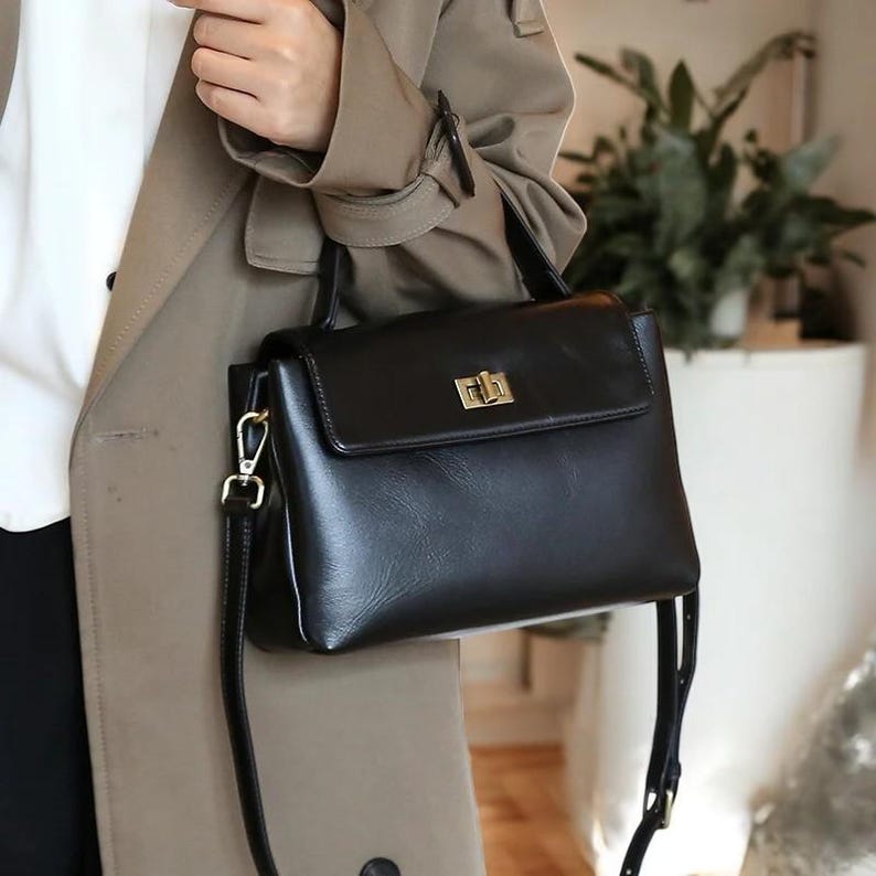 May include: A black leather handbag with a gold clasp and a long adjustable strap. The bag has a top handle and a flap closure.