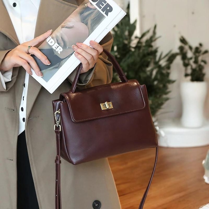 May include: A brown leather handbag with a gold clasp and a long strap. The bag has a top handle and a flap closure.
