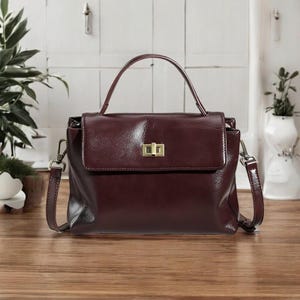 May include: A burgundy leather handbag with a top handle and a detachable shoulder strap. The bag has a gold-toned clasp closure.