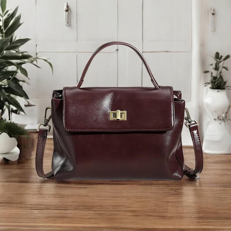 May include: A burgundy leather handbag with a top handle and a detachable shoulder strap. The bag has a gold-toned clasp closure.
