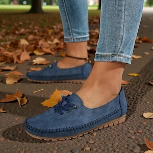 Puede incluir: Mocasines de ante azul con dise&ntilde;o cosido y suelas color canela. Los zapatos tienen cordones y se usan con vaqueros azules. La imagen est&aacute; tomada al aire libre con hojas de oto&ntilde;o esparcidas.
