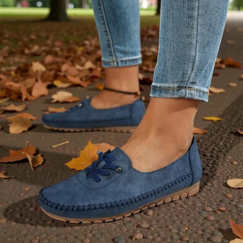 Puede incluir: Mocasines de ante azul con dise&ntilde;o cosido y suelas color canela. Los zapatos tienen cordones y se usan con vaqueros azules. La imagen est&aacute; tomada al aire libre con hojas de oto&ntilde;o esparcidas.