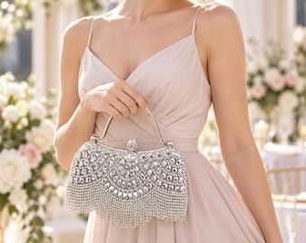 May include: A silver-toned clutch bag featuring a curved top frame, a metallic handle, and an exterior densely covered in clear, faceted crystals arranged in a scalloped pattern with a long, dangling crystal fringe along the bottom edge.