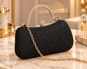 May include: A black clutch bag with a shimmering, textured surface, featuring a gold-toned metal frame, a curved handle encrusted with clear crystals, a spherical crystal clasp, and a detachable gold-toned chain shoulder strap.