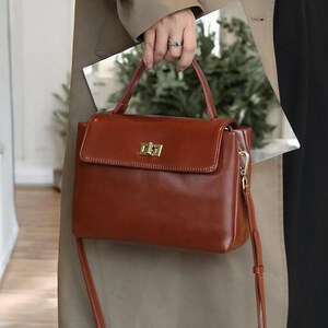 May include: A brown leather satchel handbag with a gold clasp and a long strap. The bag has a top handle and a flap closure.