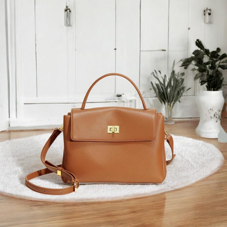 May include: A brown leather satchel handbag with a top handle and a long adjustable shoulder strap. The bag has a gold metal clasp closure.