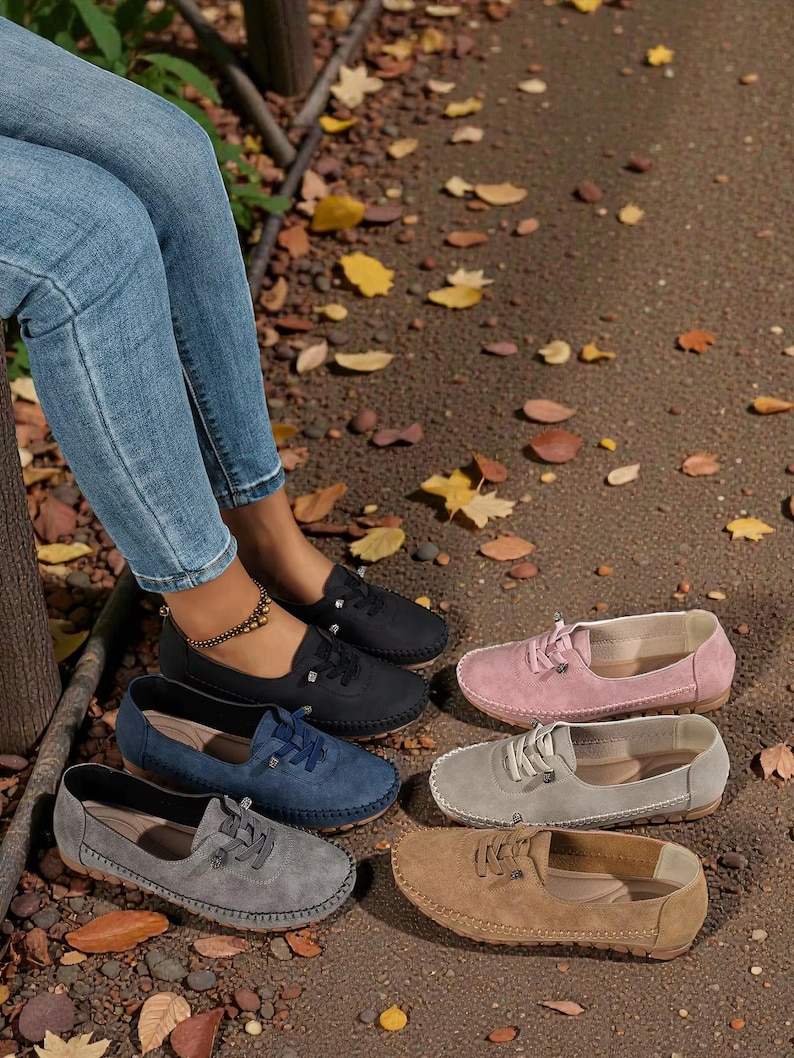 Puede incluir: Se muestran varios zapatos sin cordones de ante en negro, azul marino, gris, rosa y marr&oacute;n. Los zapatos informales tienen cordones y una puntera redonda. La imagen tambi&eacute;n muestra a una persona que lleva vaqueros azules.
