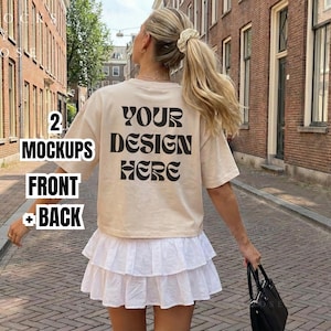 May include: A beige t-shirt with the text "YOUR DESIGN HERE" in black, paired with a white tiered skirt. The image also includes text that says "2 MOCKUPS FRONT + BACK". The person is holding a black handbag.