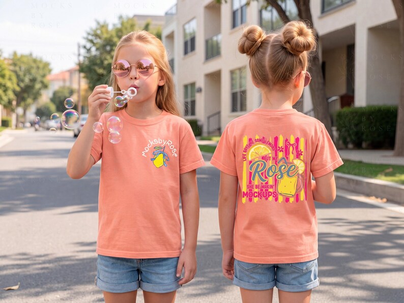 May include: Two young girls wearing peach-colored t-shirts and denim shorts stand on a street. One blows bubbles, while the other's shirt features a graphic with the text "Rose" and "She Be Makin' Mockups."