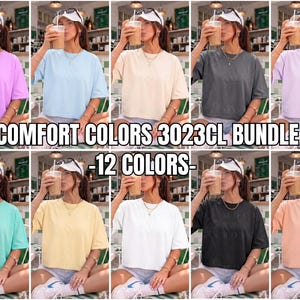 Könnte beinhalten: Eine Auswahl von zwölf kurzärmeligen T-Shirts in verschiedenen Farben, darunter Lavendel, Hellblau, Creme und Schwarz. Der Text "COMFORT COLORS 3023CL BUNDLE - 12 COLORS-" ist im Bild zu sehen.