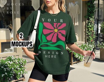 Può includere: T-shirt verde scuro con un grande disegno floreale in rosa, giallo e verde. Il testo "YOUR DESIGN HERE" è stampato sotto il fiore. Le parole "2 MOCKUPS" sono stampate in bianco sul lato sinistro della maglietta.