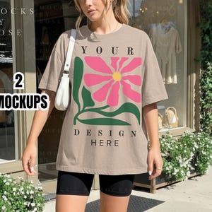 Peut inclure: T-shirt beige avec un grand motif de fleur rose et l'inscription "YOUR DESIGN HERE". L'image comprend également le texte "2 MOCKUPS". Le modèle porte un short noir et un sac à main blanc.