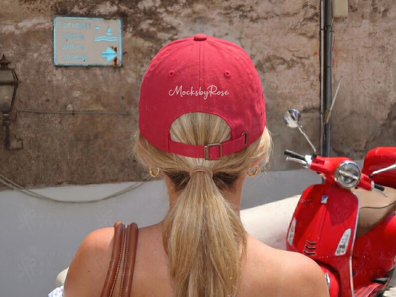 May include: A red baseball cap with the text "MocksbyRose" on the back. The cap has a curved brim and an adjustable strap. A red scooter is parked nearby.