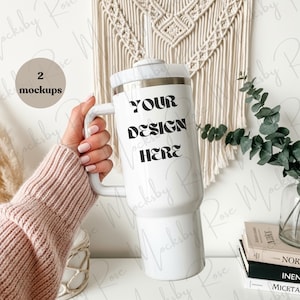 Puede incluir: Un vaso blanco con asa, con el texto "YOUR DESIGN HERE" en negro. El vaso lo sostiene una persona que lleva un suéter rosa. El fondo incluye un tapiz de macramé y vegetación.