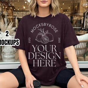 Pode incluir: Uma t-shirt bordô com o texto "MOCKSBYROSE" e "YOUR DESIGN HERE" em branco. A t-shirt apresenta um gráfico de limão e as palavras "ESTD 2025". A imagem também inclui o texto "2 MOCKUPS" numa caixa branca.