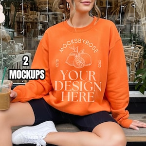 Könnte beinhalten: Orangener Sweatshirt mit weißem Grafikdesign mit der Aufschrift "Mocksbyrose" und "Your Design Here". Das Bild enthält auch den Text "2 Mockups". Das Model trägt schwarze Shorts und weiße Turnschuhe.