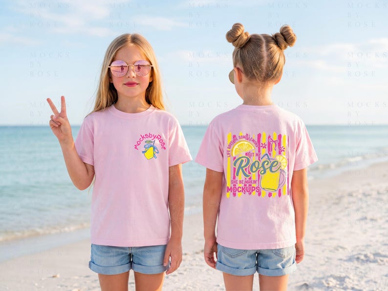 May include: Two young girls wearing pink t-shirts with graphic designs, standing on a beach. One shirt has a lemon graphic and the text "mocksbyrose". The other shirt has a lemon and text that says "Life gives you lemons but make Rose the best in mockups".