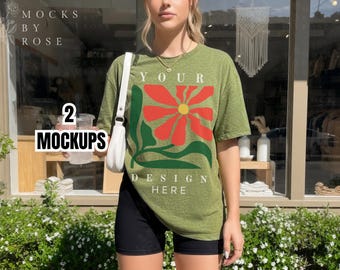 Può includere: T-shirt verde oliva con un grande disegno floreale rosso, verde e giallo. Il testo "YOUR DESIGN HERE" è stampato sotto il fiore. La modella indossa pantaloncini neri e una borsa bianca.