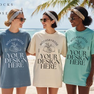 May include: Three people wearing oversized t-shirts on a beach. The shirts are in blue, cream, and teal, each with a circular logo and the text "YOUR DESIGN HERE". The logo includes a fruit illustration and the text "MOCKSBYROSE".