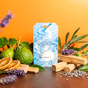 May include: A rectangular, blue and white marbled tag with a geometric hummingbird design and the text "BOHEMIAN I". The tag is surrounded by fresh green limes, dried orange slices, lavender, and wooden incense sticks against an orange background.