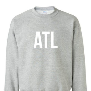 Puede incluir: Sudadera gris jaspeada con las letras blancas "ATL" en el pecho. La sudadera tiene cuello redondo, mangas largas y puños y dobladillo de canalé. El logotipo de la marca es visible en el interior del cuello.