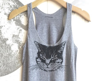 Può includere: Canotta grigia con un'illustrazione in bianco e nero di un viso di gatto. Il testo "Anewlark" è stampato sul retro della canotta.