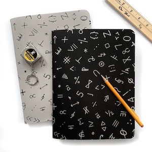 May include: Two notebooks with black and white geometric patterns. The notebook on the left is gray with white patterns. The notebook on the right is black with white patterns. A yellow pencil is lying on top of the black notebook.