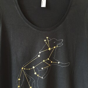 May include: Black scoop-neck t-shirt featuring a gold constellation design of a wolf. The wolf is outlined with small white dots, and the stars are connected by gold lines. The shirt has a tag that reads "American Apparel".