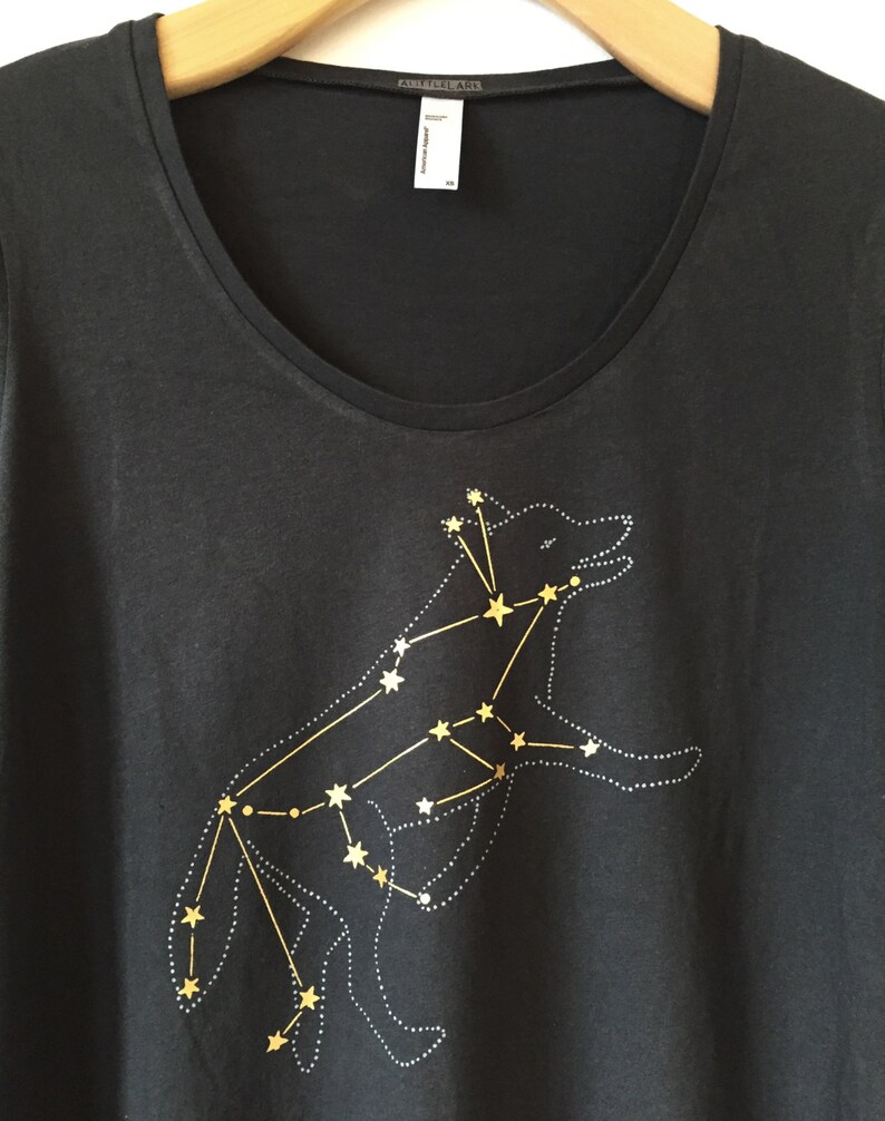 May include: Black scoop-neck t-shirt featuring a gold constellation design of a wolf. The wolf is outlined with small white dots, and the stars are connected by gold lines. The shirt has a tag that reads "American Apparel".