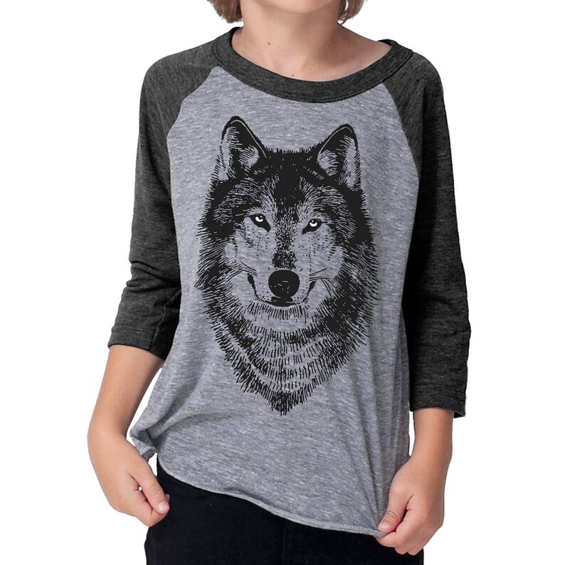 Puede incluir: Una camiseta de b&eacute;isbol gris y negra con una ilustraci&oacute;n en blanco y negro de la cara de un lobo en la parte delantera.