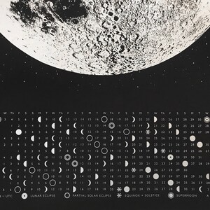 May include: A black and white calendar featuring a full moon with a detailed surface texture. The calendar shows the phases of the moon for each day of the year 2018. The calendar also includes dates for lunar eclipses, partial solar eclipses, equinoxes, solstices, and supermoons.