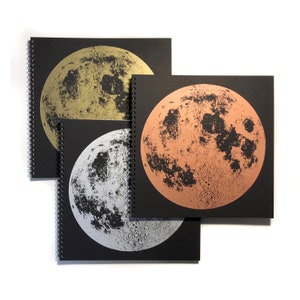 May include: Three black spiral bound notebooks with a full moon image on each cover. The moons are printed in gold, copper, and silver foil.