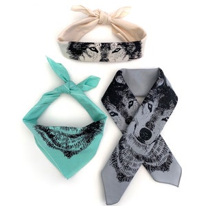 Pode incluir: Três bandanas diferentes com um design de rosto de lobo. Uma é branca com olhos de lobo pretos, outra é azul claro com um rosto de lobo preto e a última é cinza com um rosto de lobo preto.