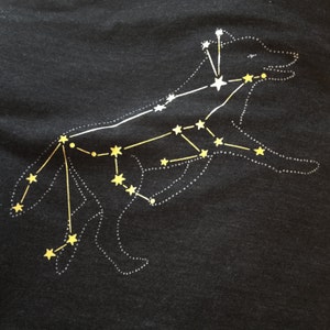 May include: A black t-shirt with a white outline of a dog constellation with yellow stars.