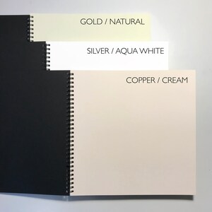 May include: Three spiral bound notebooks with different colored covers. The covers are black, cream, and aqua white. The text on the covers reads "GOLD/NATURAL", "SILVER/AQUA WHITE", and "COPPER/CREAM".