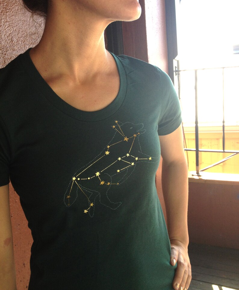 May include: A dark green t-shirt with a gold embroidered constellation design of a wolf. The design is detailed and intricate, with each star in the constellation clearly visible.